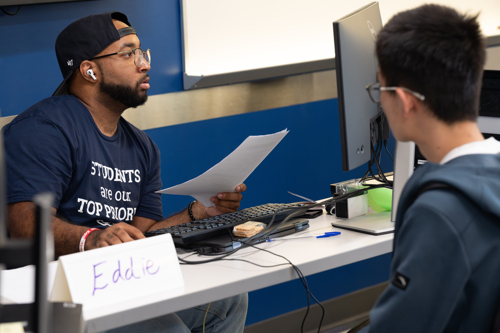 staff member sitting at a desk and computer helping a student 